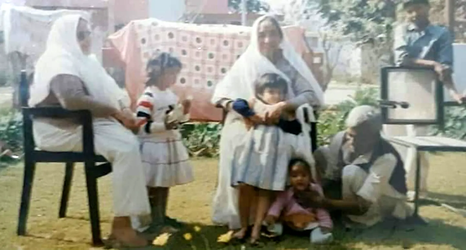 Sumati as a child sitting at Ma’s feet in a family group outdoors