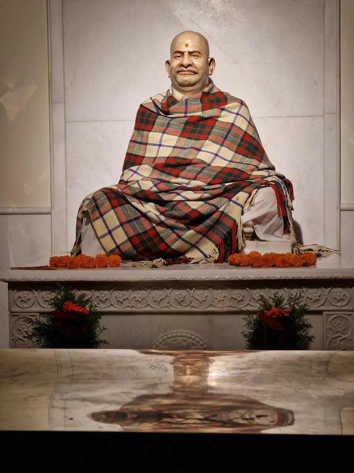 Seated statue of Neem Karoli Baba Maharajji wrapped in a checked shawl