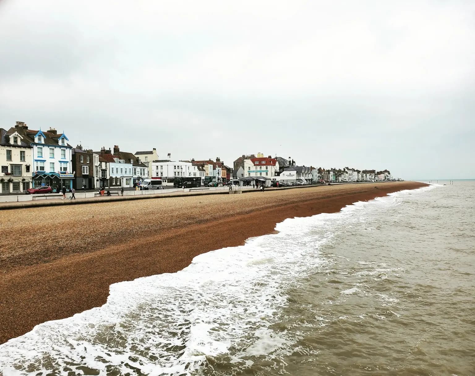 Pebble beach curving towards a coastal town beneath an overcast sky
