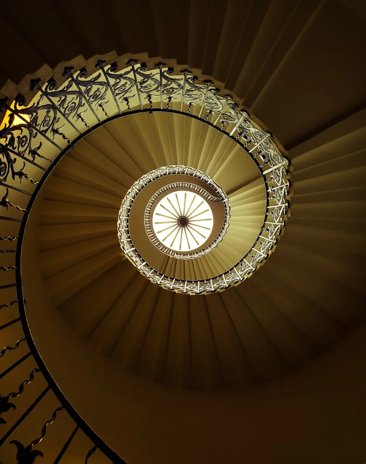 Ornate spiral staircase curling towards a circular skylight