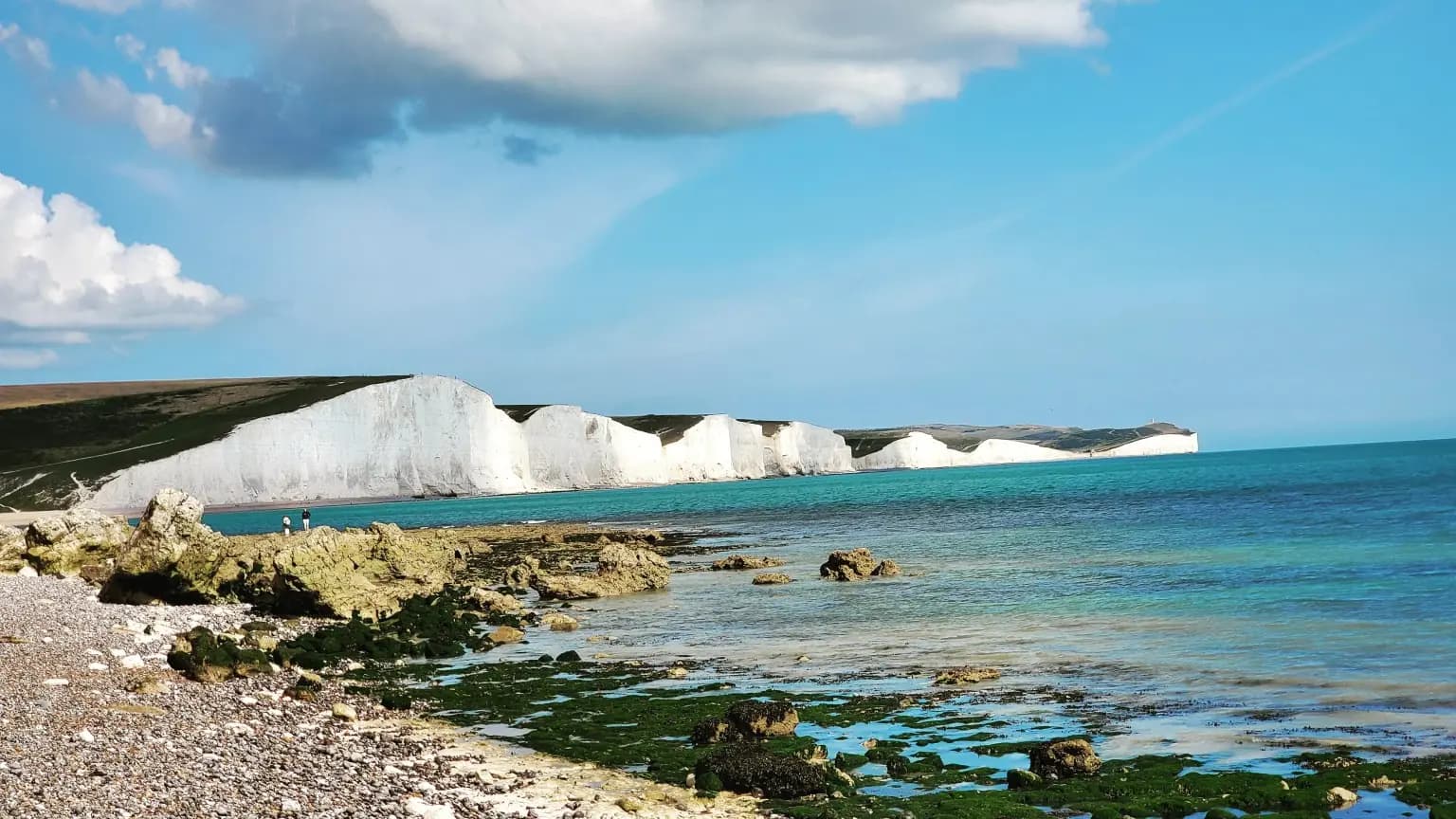 White chalk cliffs across turquoise water and a rocky shore